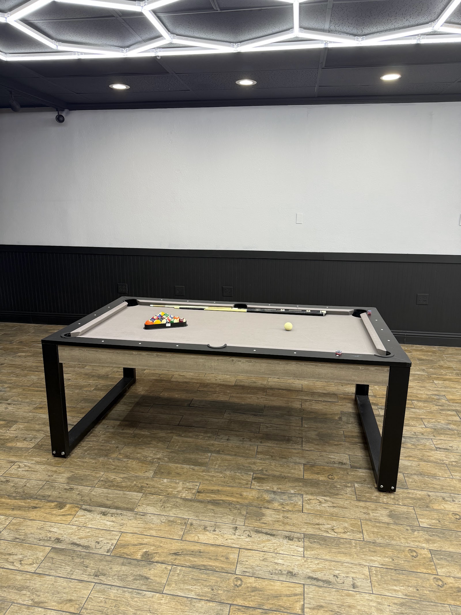 Pool table with balls and cues in the barbershop lounge area under hexagonal lights